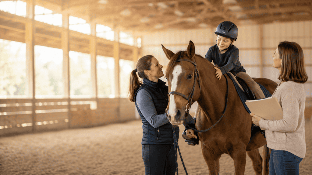 Child riding a calm therapy horse with an instructor and parent nearby in a warm indoor arena.